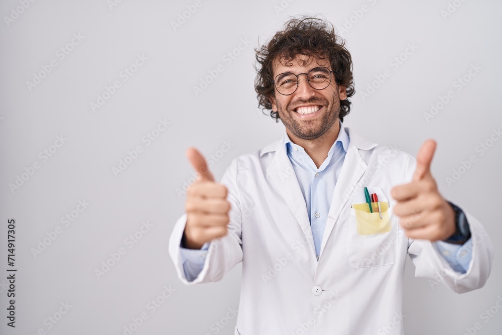 Sticker hispanic young man wearing doctor uniform success sign doing positive gesture with hand, thumbs up s