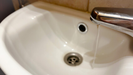 Pure water pouring into white ceramic basin in the bathroom. Modern conveniences at home. Film...
