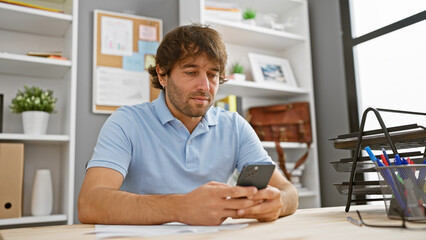 Handsome caucasian man with beard checking smartphone at modern office desk