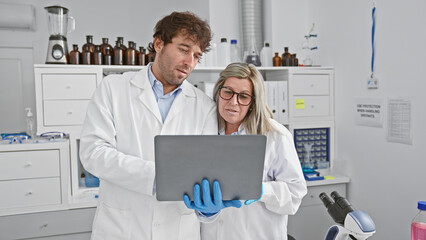 Two dynamic scientists, a man and woman, working together with a laptop in the buzzing lab