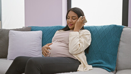 Radiant young pregnant woman engrossed in listening to adorable voice message on smartphone,...