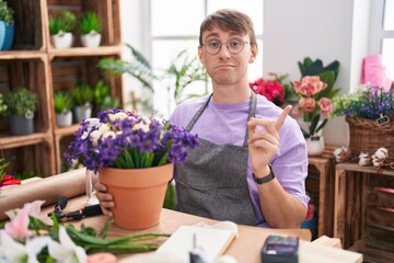 Caucasian blond man working at florist shop pointing aside worried and nervous with forefinger,...