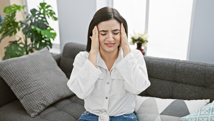 A young hispanic woman experiencing headache in a cozy modern living room.