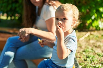 Mother and son sitting on bench together eating little worms snack at park