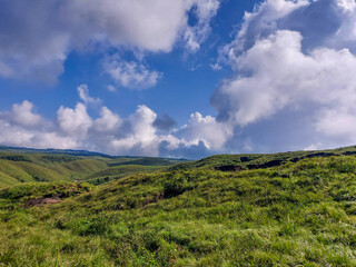 Green landscaped mountain amid blue sky with a beautiful view of cumulus Cloudscape.