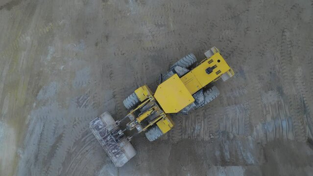 Aerial view of a yellow excavator parked in a gravel quarry. Camere slides forward.