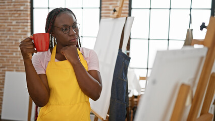 Serious african american woman artist, with beautiful braids and glasses, holding a coffee cup and...