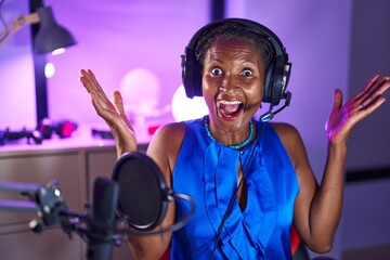 African woman with dreadlocks wearing headphones celebrating victory with happy smile and winner...