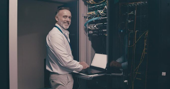 Portrait of mature man in server room with laptop, network maintenance and engineer in digital storage for update. Tech, system administration and happy technician online in data center with computer