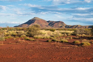 Beautiful mountain landscape in Karijini National Park, Western Australia. Red colored soil of Australias outback in front of a bush land and mountains in the background. Western Australia road trip. 