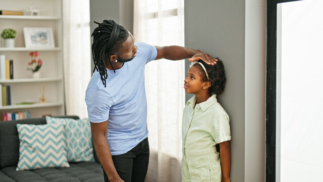 African american father and daughter smiling confident measuring height on wall at home - Powered by Adobe