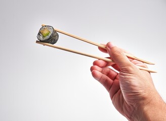 A man's hand skillfully holds a sushi roll with chopsticks against a white background, illustrating...