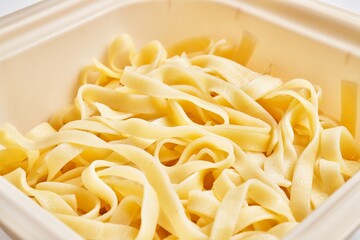 Close-up of fresh fettuccine pasta in a white container highlighting italian cuisine and homemade cooking.