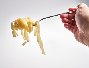 Close-up of a hand twirling fettuccine pasta on a fork against a white background, depicting...