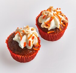 Two frosted carrot cupcakes in red liners on a white background, tempting and ready to eat.