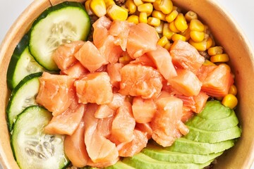 Close-up of a colorful poke bowl featuring salmon, avocado, cucumber, and corn served in a disposable bowl, illustrating a healthy meal option.