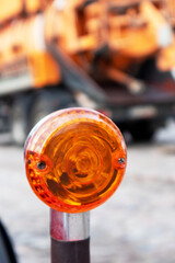 
An orange car lamp on a red car wing on the background of a heavy machine