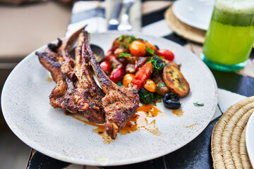 Grilled lamb chops on a ceramic plate with vegetables and a green smoothie at a laid-back outdoor setting.