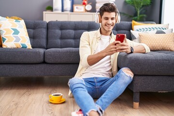 Obraz premium Young hispanic man listening to music sitting on floor at home