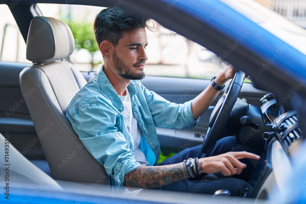 Wall mural young hispanic man sitting on car turning on radio at street