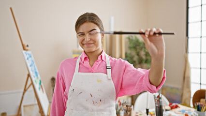 Vibrant young hispanic female artist, radiating confidence and joy, paintbrush in hand creating magic at the heart of an art studio