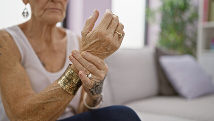 Elderly woman with short grey hair, suffering wrist pain, sitting on sofa at home