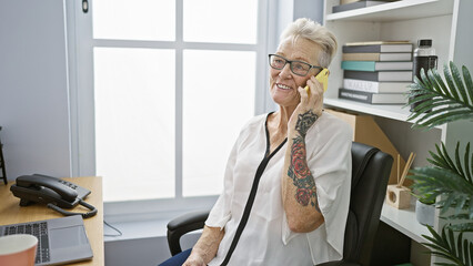 Confident senior grey-haired woman boss, happily talking on phone, conquering business success at...