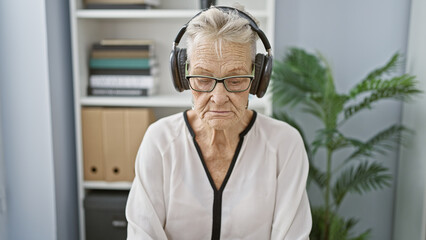 Elegant grey-haired senior woman worker relaxing, listening to soothing music while working hard at office job