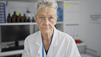 Senior grey-haired woman scientist sitting with serious face at laboratory