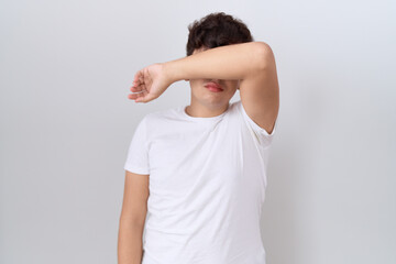 Young non binary man wearing casual white t shirt covering eyes with arm, looking serious and sad....