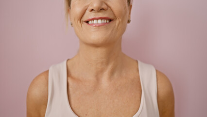 A smiling middle-aged woman with blonde hair against a pink isolated background portraying...