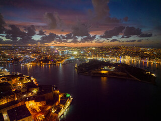 Beautiful Valletta coastline lights with reflection on the sea at sunset with pink sky. Aerial panoramic view towards Manoel Island and Sliema.