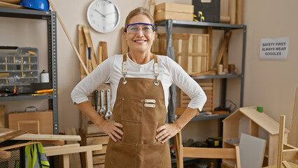 Smiling woman in apron posing in a cluttered carpentry workshop, indicating craftsmanship and...