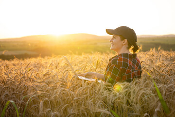 Fototapeta premium Woman farmer working with laptop on wheat field. Smart farming and digital agriculture