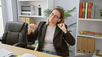 Blonde bombshell boss lady, young business workaholic caught dancing joyfully to her favorite tune at the office, electrifying the air with positivity while juggling professional duties