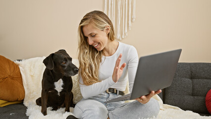 A caucasian woman enjoys a video call at home with her dog and laptop, showcasing companionship and technology in a cozy setting. - obrazy, fototapety, plakaty