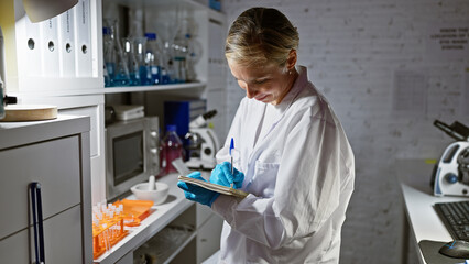 Blonde woman scientist writing in notebook while working in a modern laboratory.