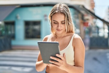 Young blonde woman smiling confident using touchpad at street