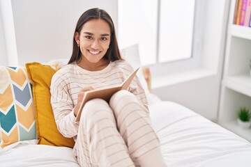 Young beautiful hispanic woman writing on notebook sitting on bed at bedroom