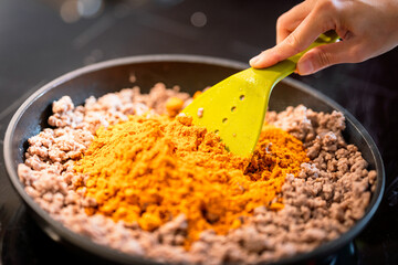 adding spices to mince meat in frying pan.