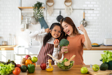 Portrait of enjoy happy love asian family mother and little asian girl daughter child having fun help cooking food healthy eat together with fresh vegetable salad and ingredient in kitchen