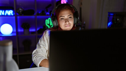 Focused young redhead woman streamer, engrossed in intense gaming session, in a serious virtual...