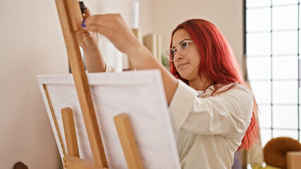 Vibrant young redhead artist, full of creativity, joyfully preparing to paint, standing in the midst of her art studio, ready to put canvas on easel and draw her masterpiece