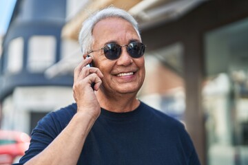 Middle age grey-haired man smiling confident talking on the smartphone at street