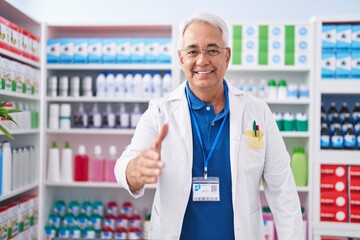 Middle age grey-haired man pharmacist smiling confident shake hand at pharmacy
