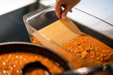 making lasagna, adding pasta to mince meat in ovenproof dish.