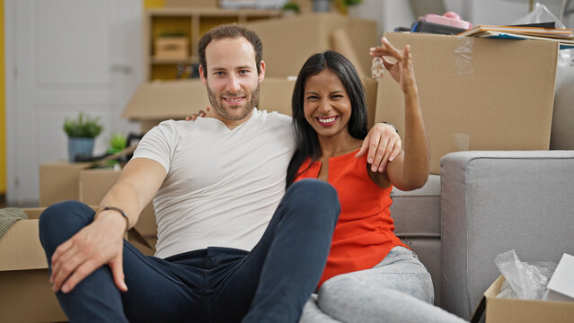 Beautiful couple sitting on floor together holding keys at new home