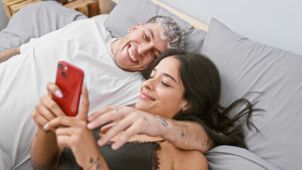 Obraz na płótnie Canvas A couple shares a joyful moment taking a selfie in a cozy bedroom, radiating love and happiness together