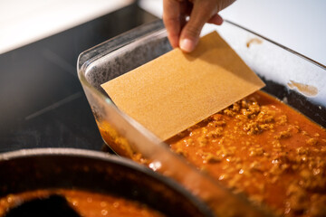 making lasagna, adding pasta to mince meat in ovenproof dish.