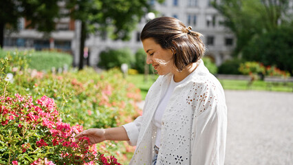 Beautiful young hispanic woman looking at flowers at the park